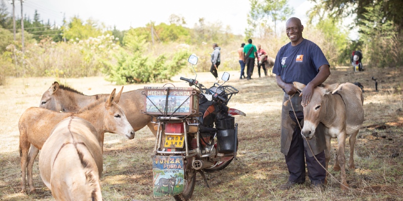 A man, john the farrier, standing next to his motorbike and surrounded by donkeys