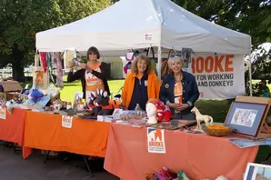 An orange tablecloth with the Brooke logo covers a stall with a white tent, as a group of fundraisers sell crafts