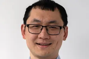 Bo Ruan smiling in a blue and white checked shirt, in front of a white background