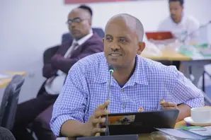 Tewodros sits at a desk in a blue shirt.