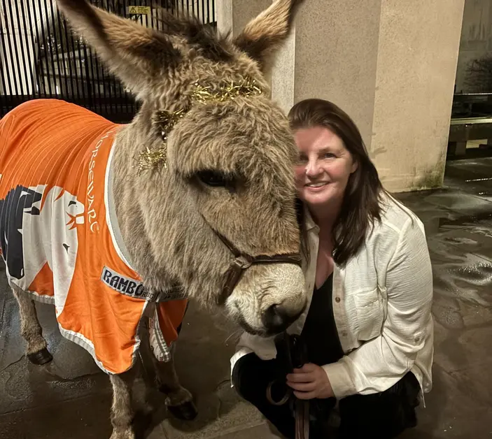 Emma Johnson kneels down next to a donkey in a Brooke blazer