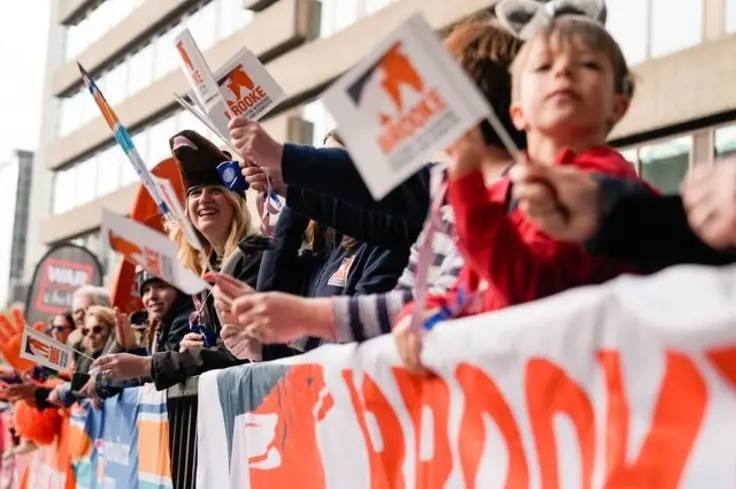 A crowd stand behind a Brooke banner, waving Brooke flags at a marathon